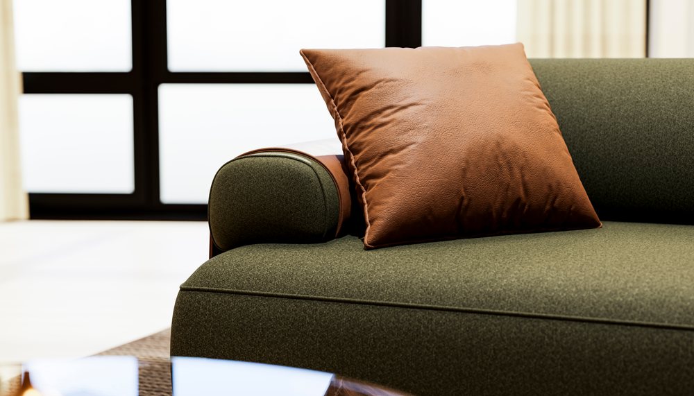 Brown cushion placed on a green upholstered sofa armrest with leather detail in a modern living room.