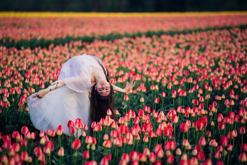 Woman bending backward in a vibrant pink tulip field outdoors in the USA at sunset.