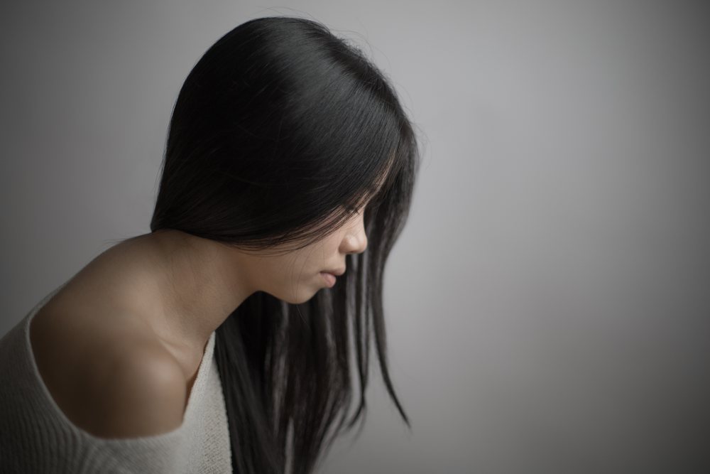Portrait of an emotional woman with black long hair in soft studio light looking downward in a minimalist setting.