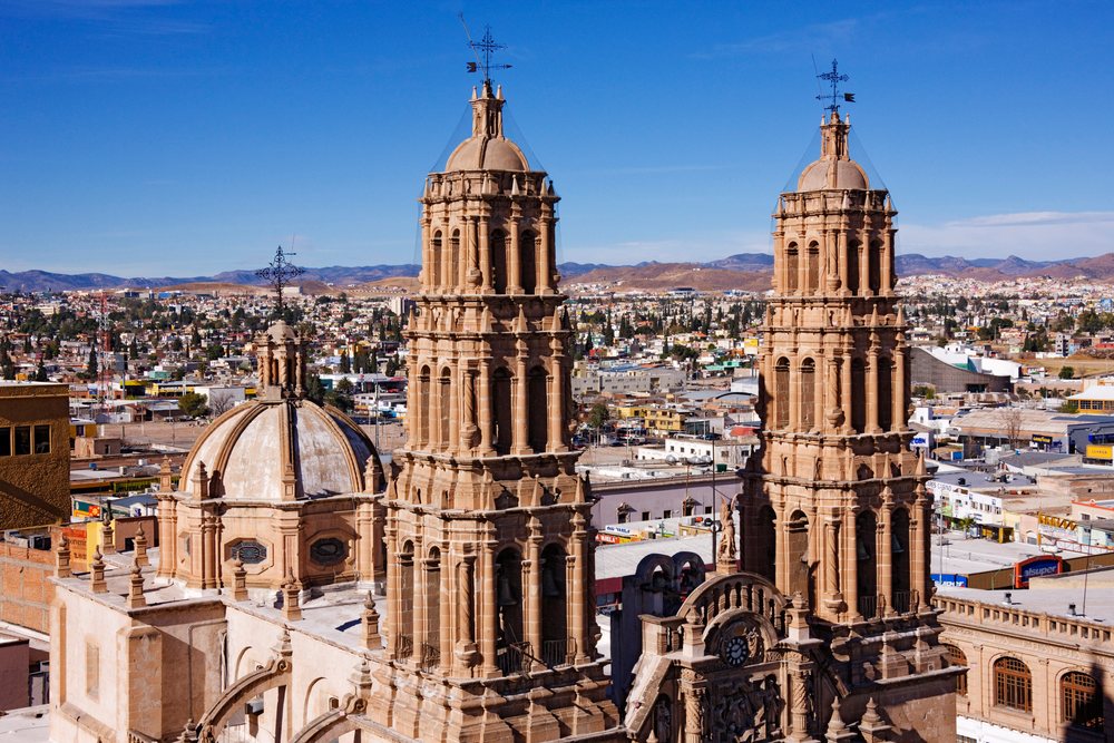 Metropolitan Cathedral Church towers and dome overlook Chihuahua cityscape with mountains under clear blue sky, Mexico.