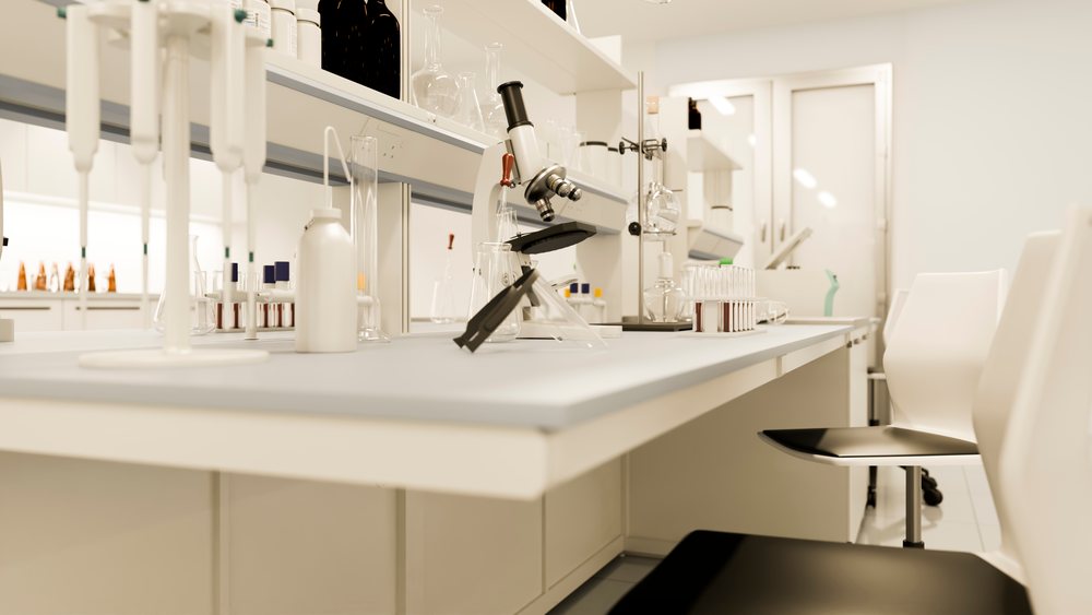 Microscope, test tubes, pipettes, and beakers arranged on a white laboratory bench with chairs in a research facility.