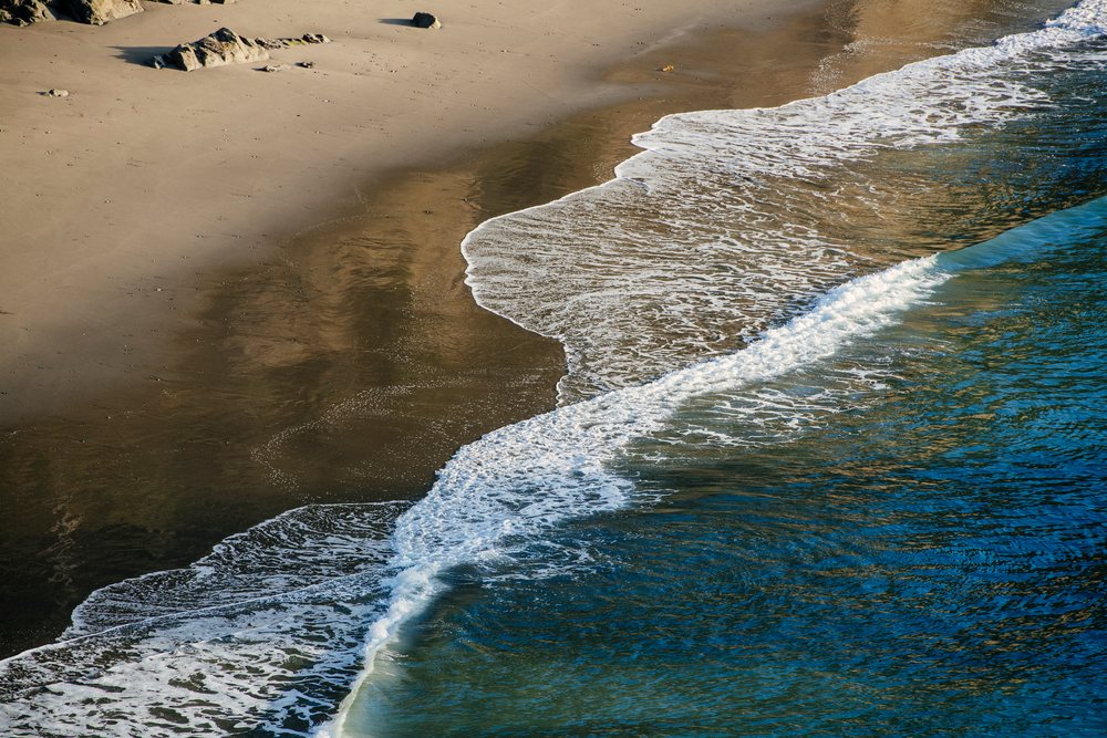 Ocean waves with white foam wash onto the sandy beach with rocks, Boardman State Park, Oregon, USA.