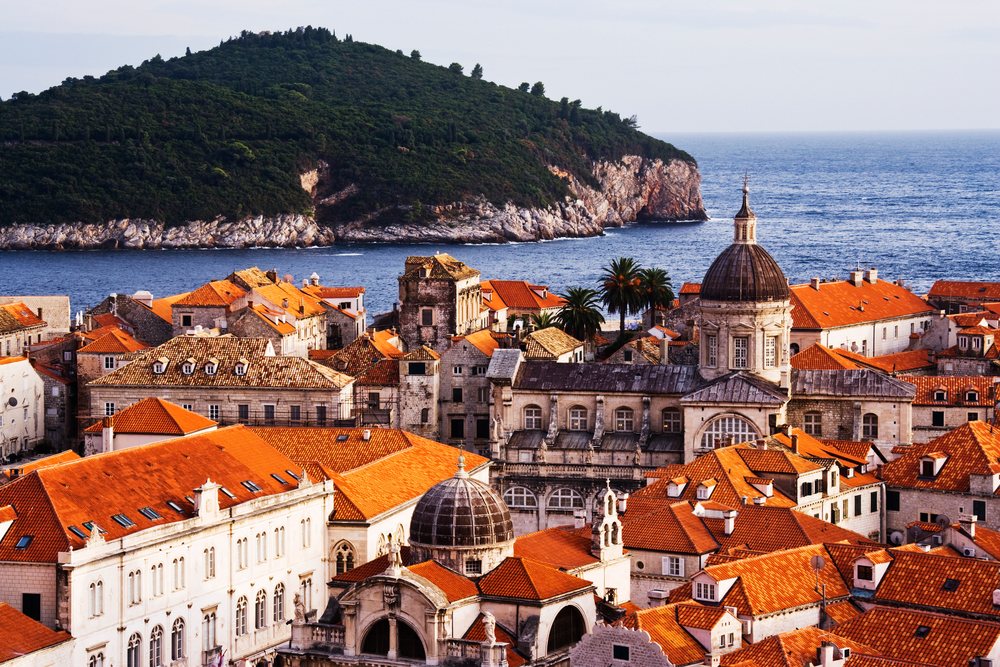 Historic old town of Dubrovnik with red tiled roofs and a church dome, by the Adriatic Sea and green Lokrum Island.