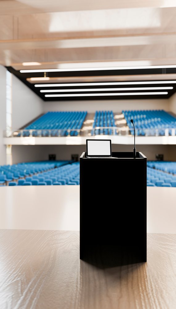 Podium with laptop and microphone in an empty modern lecture hall.