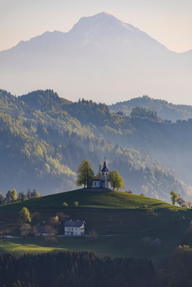 St Thomas's Church with conical roof stands on a grassy hilltop, landscape, cityscape, Škofja Loka, Slovenia.