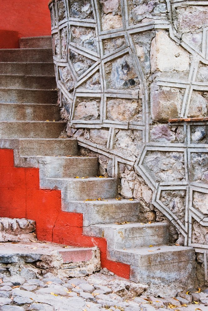 Outdoor stone steps with red painted edges ascend beside a rough textured stone masonry wall, Guanajuato, Mexico.