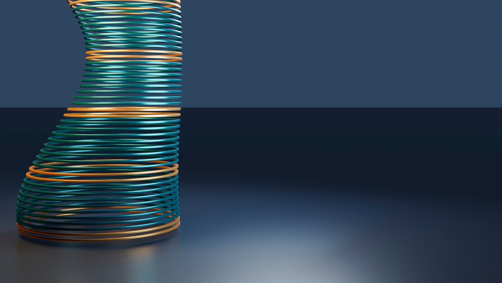 Colorful spiral metal coil sculpture composed of interlocked blue, gold, orange, and teal rings against a solid blue background in a minimalist studio setting.