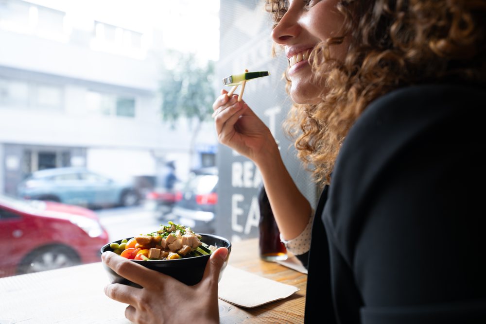 Woman enjoying a healthy bowl meal using chopsticks at an urban cafe, businesswoman, traveling executive, Spain.