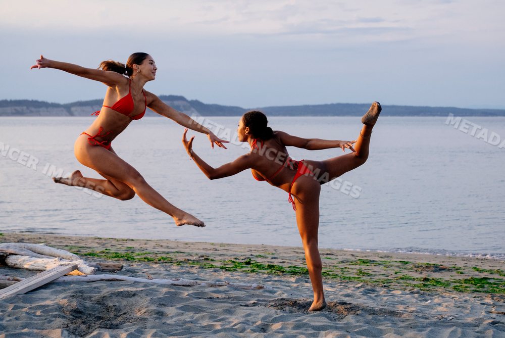 Two women practicing partner acrobatics yoga on a beach in wa USA