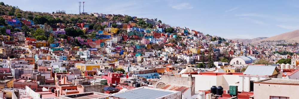 Panoramic view of colorful hillside houses city, Mexico, under a clear blue sky.