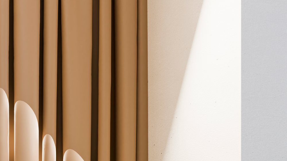 Abstract curtains with vertical folds cast sculptural shadows on a beige and white wall under natural light.