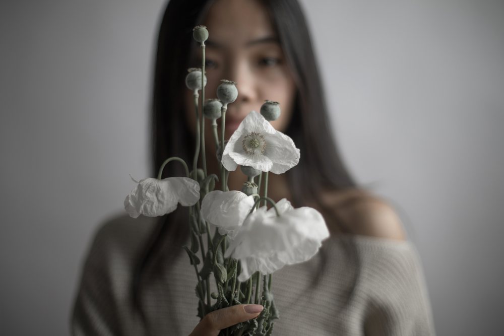 Woman holding a bouquet of white poppy flowers with seed pods against a gray background indoors, Art, portrait, emotional.