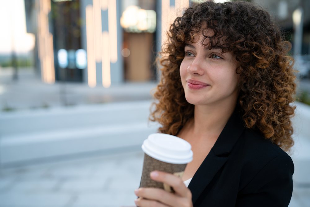 Young woman smiling and holding a coffee cup outdoors in an urban area, Madrid.