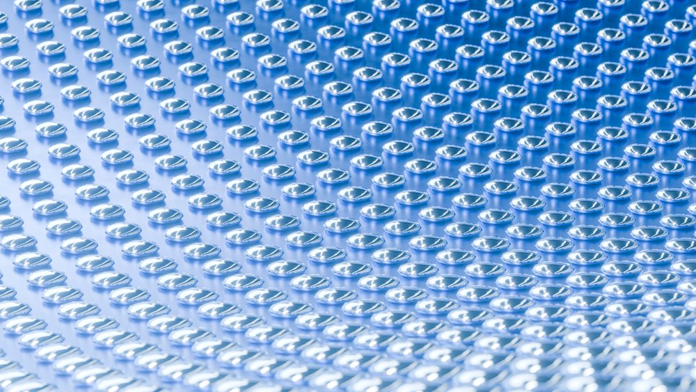 Close-up of numerous blue medicine capsules closely arranged on a reflective blue surface.