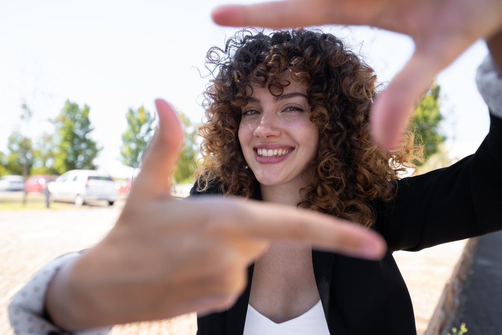 Smiling woman with curly hair, wearing a casual business outfit, outdoors in a park, businesswoman, traveling executive, Spain.