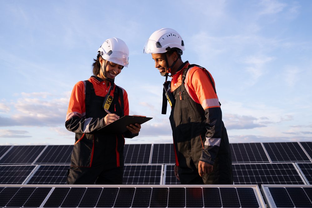 Two workers wearing safety helmets inspect solar panels outdoors at a solar energy installation site, Madrid, Spain.