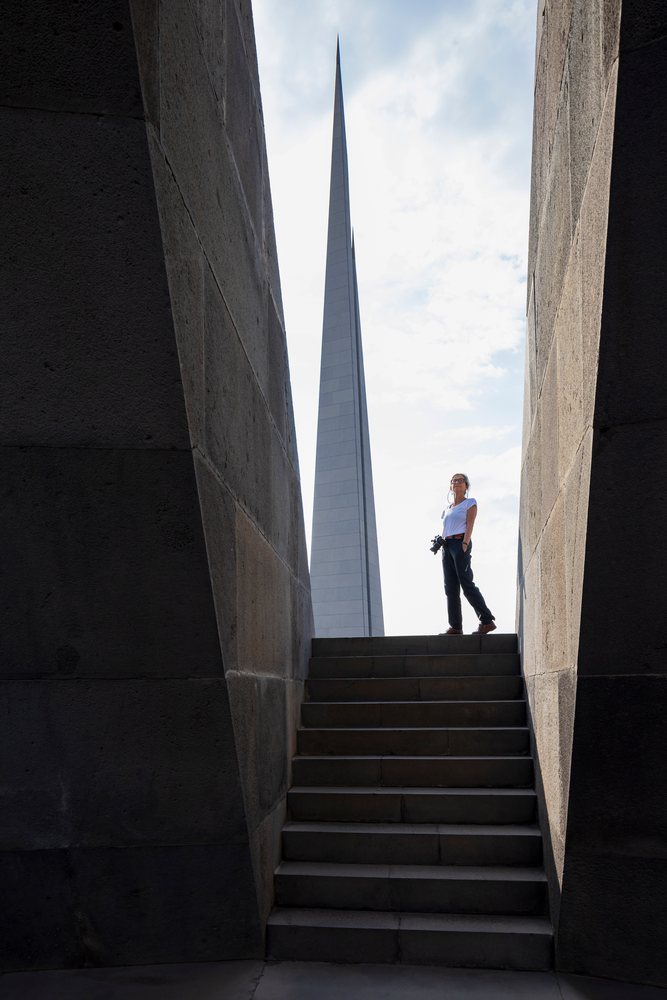 Woman tourist with a camera stands near the Armenian Genocide Memorial stairs by the tall pointed spire at Tsitsernakaberd, Yerevan, Armenia.