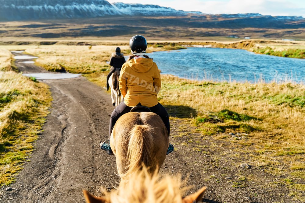 Two white women horseback riding on a trail beside a river