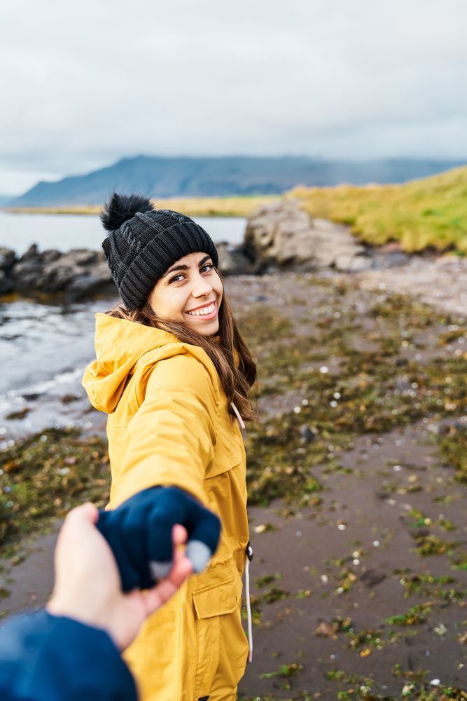 White Woman holding hand walking along the rocky coastal shore