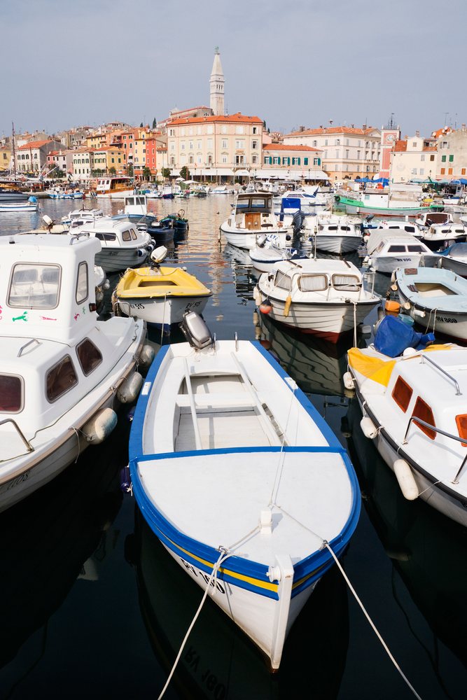 Boats moored in the harbour with colorful buildings and a tower in the background, Rovinj, Croatia.