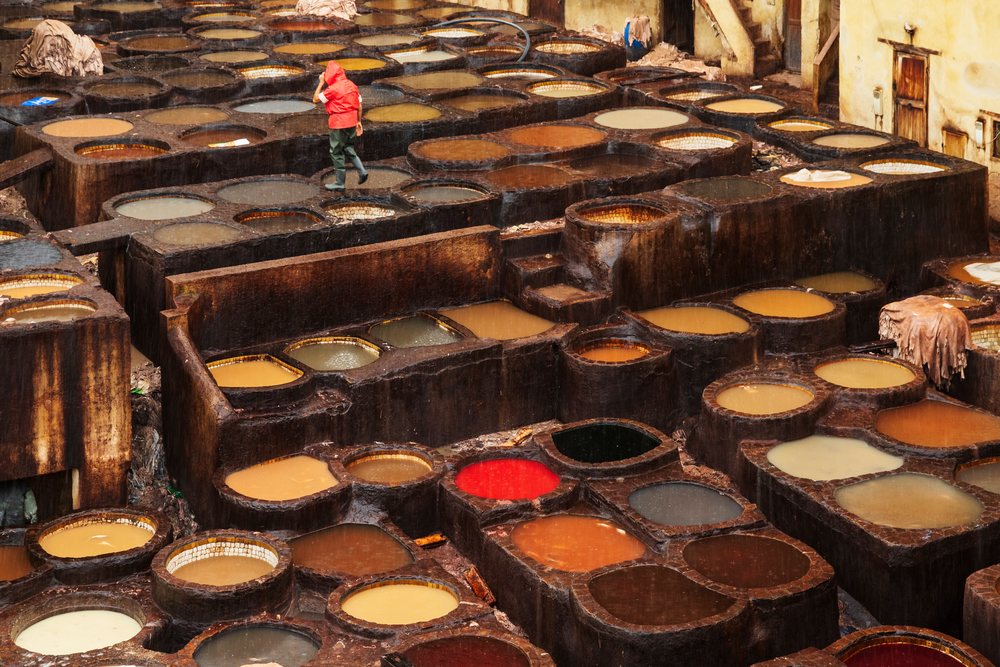 Tannery worker in a red raincoat walks among colorful dyeing pits during Pouring Rain, Landscape, Lifestyle, Fes, Fes-Meknes Administrative Region, Morocco.