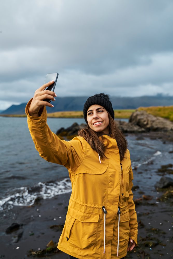 A white woman taking a selfie on the rocky coastline