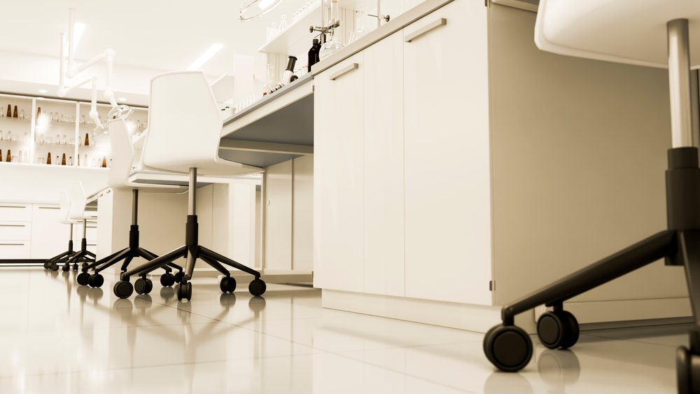 Modern laboratory interior with wheeled chairs and scientific instruments arranged on white counters.