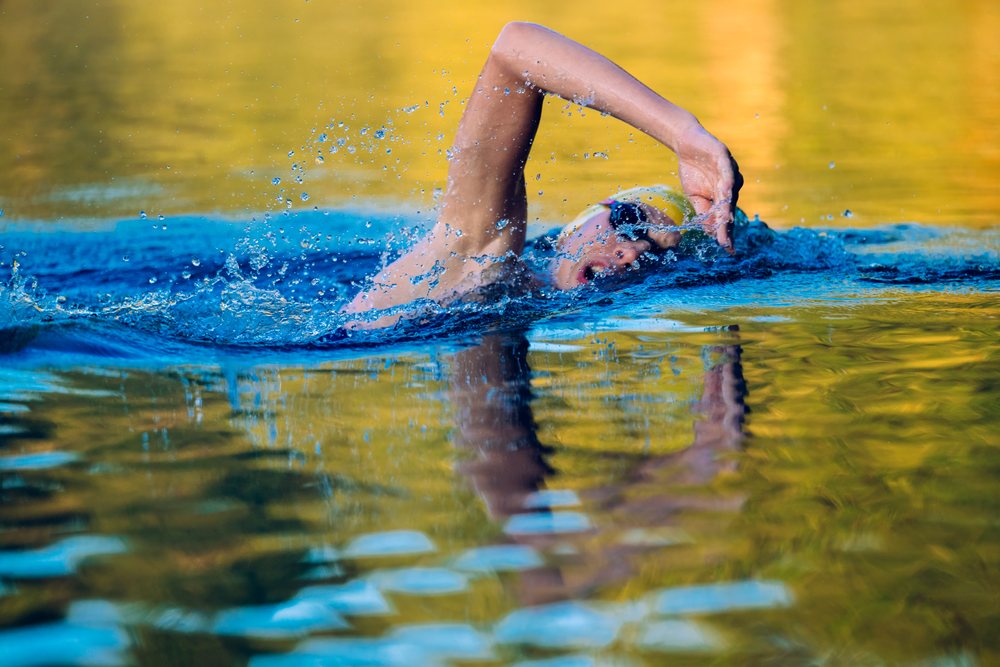 Swimmer performing open water freestyle stroke with splash in yellow and blue water, USA.