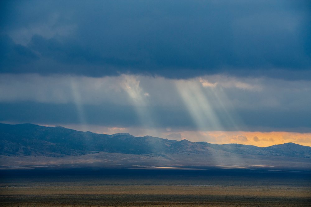 Rays of sunlight break through a cloudy sky over a mountain range and desert plain, Nevada, USA.