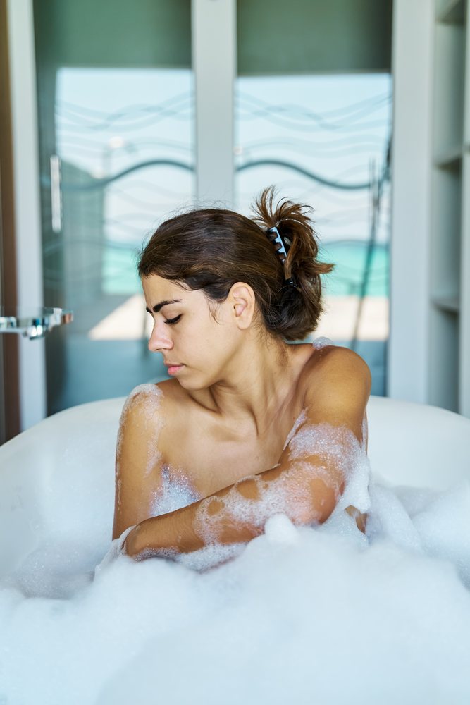 A young woman relaxes in a bubble bath in a modern bathroom with a view in the, Maldives.