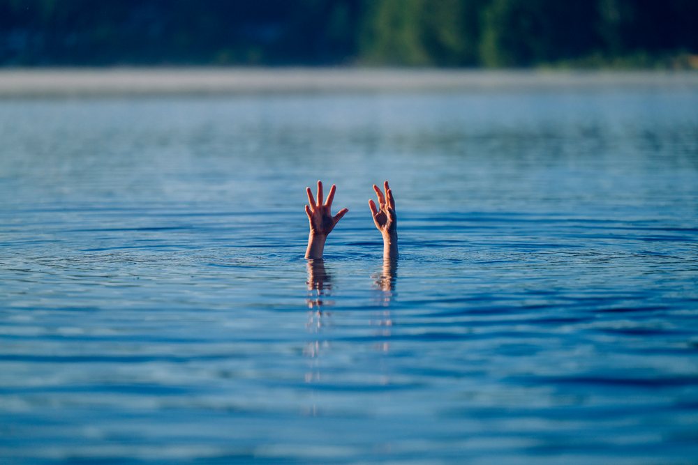 Hands of a person struggling and reaching out of a lake surface, USA.