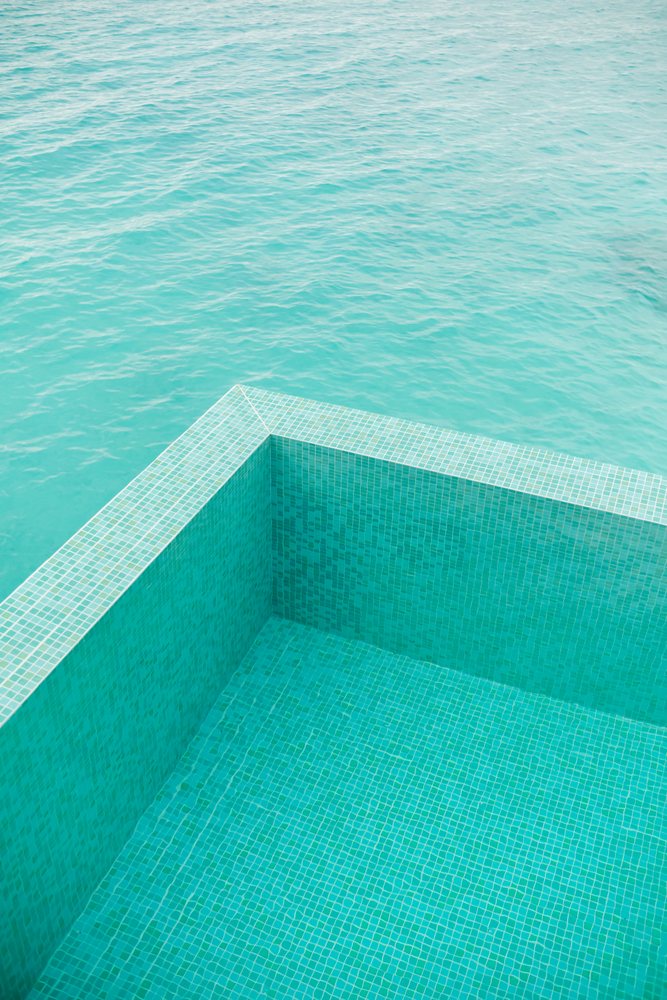 Turquoise tiled pool edge blending into calm sea water