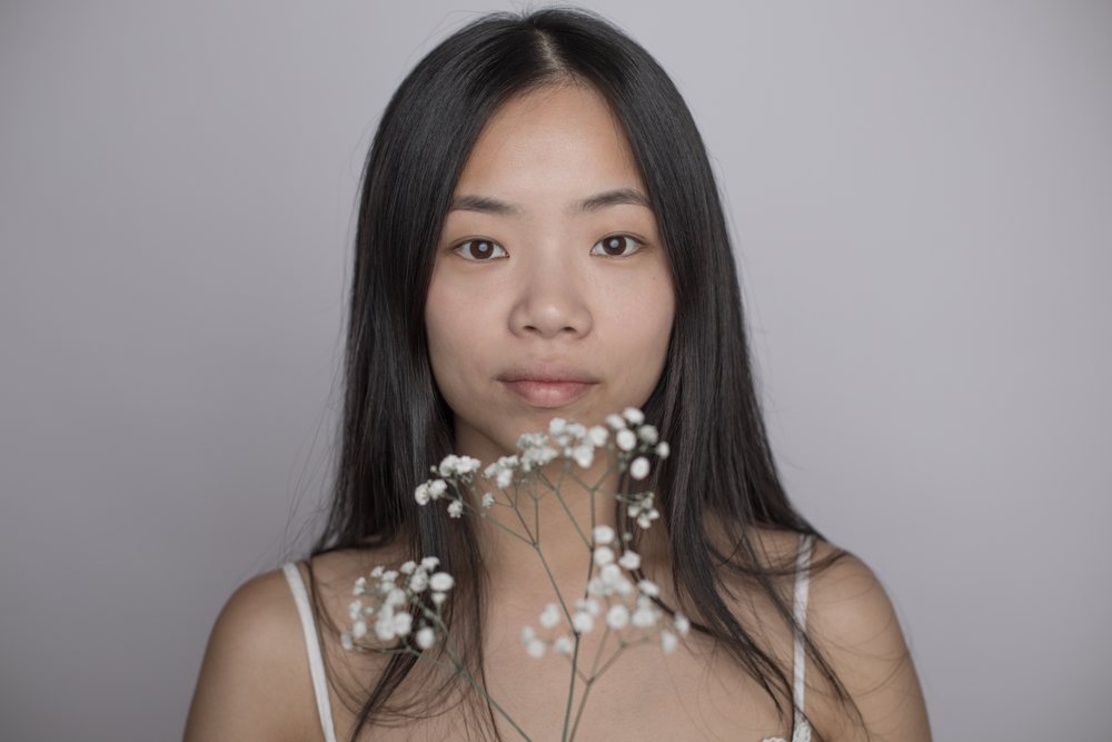 Closeup portrait of a young Asian woman holding a delicate white gypsophila flower against a neutral background with a calm, soft expression, Art, emotional.