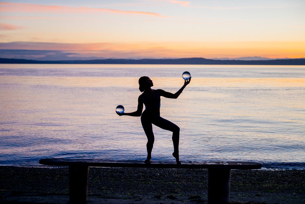 Woman balances on a bench while holding glass spheres on a beach at sunset, yoga, acrobatics, USA.