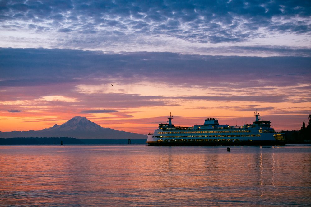 Seattle ferry sailing across calm water at sunset with Mount Rainier visible behind, Bainbridge Island, WA, USA.