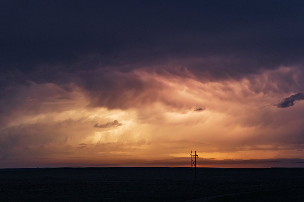Lightning Storm with dark Storm Clouds and a lightning bolt at sunset over flat horizon and power transmission lines, Alzada, Montana, USA.