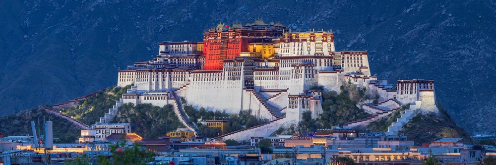 Potala Palace illuminated at Dusk on a hill overlooking Lhasa city in the Autonomous Region of Tibet with mountains in the background.