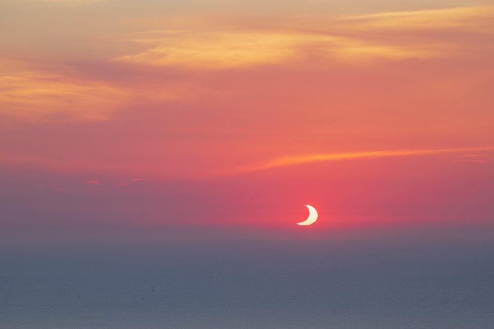 Sun partially eclipsed at sunset over a calm sea with sailboats, Landscape, Lifestyle, Valldemossa, Mallorca, Spain.