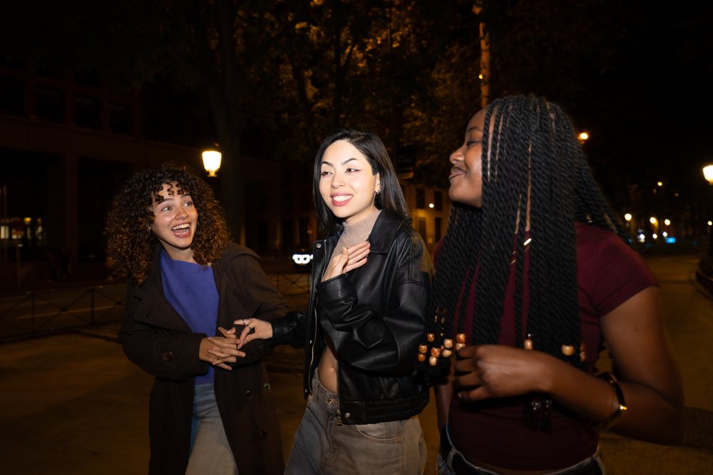Three women socialize and smile while walking on a street at night, Madrid, Spain.