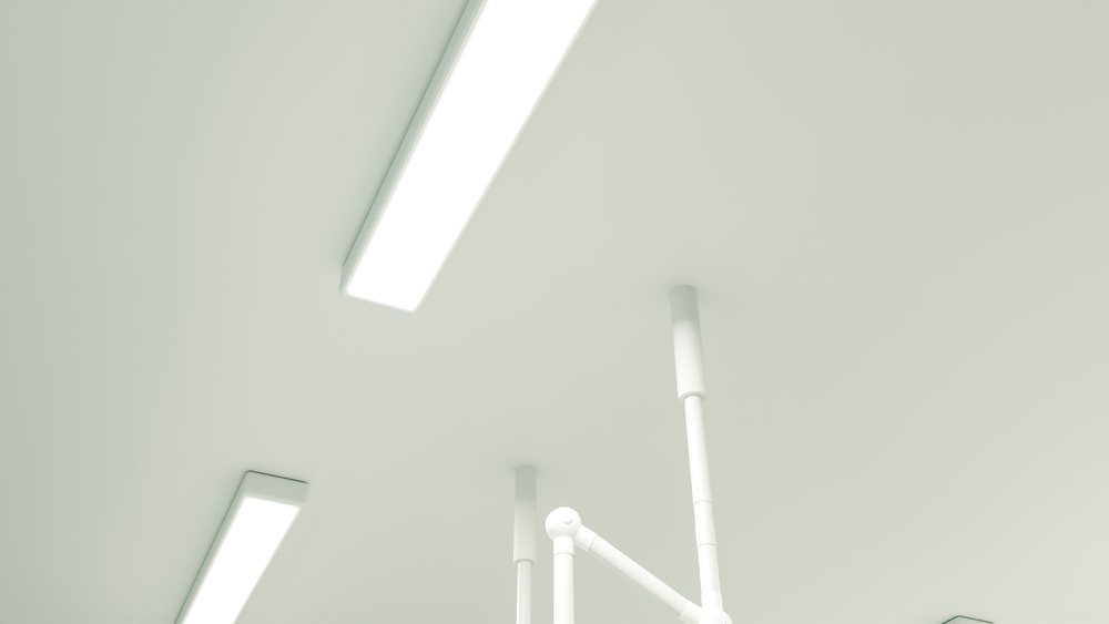 Fluorescent lights and surgical light arms mounted on a white medical ceiling in a clean clinical environment.