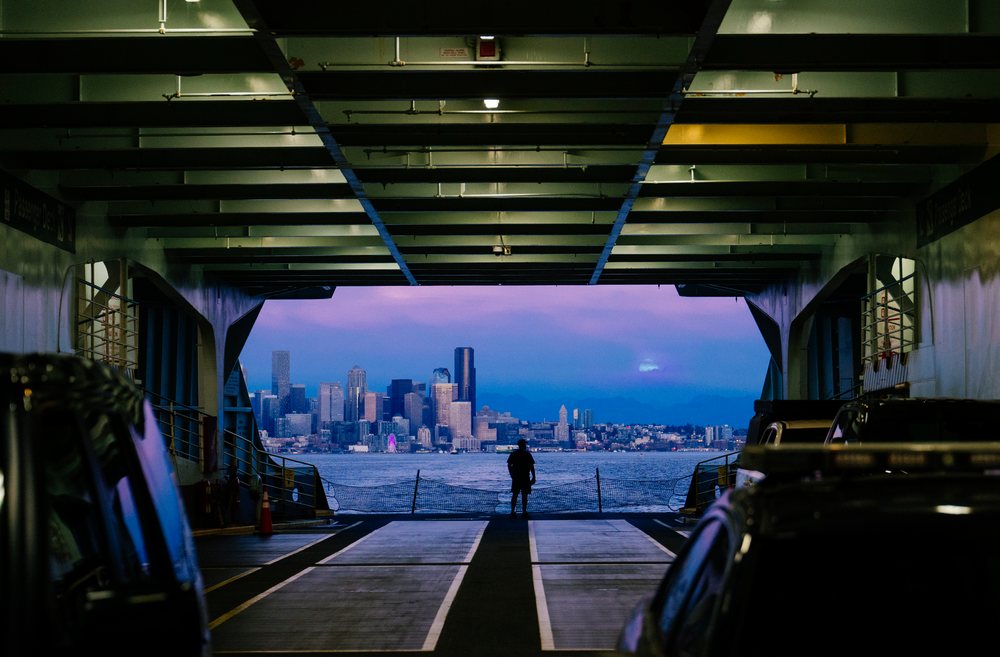 Person standing on a ferry deck looking out at a city skyline over Puget Sound at twilight, USA.