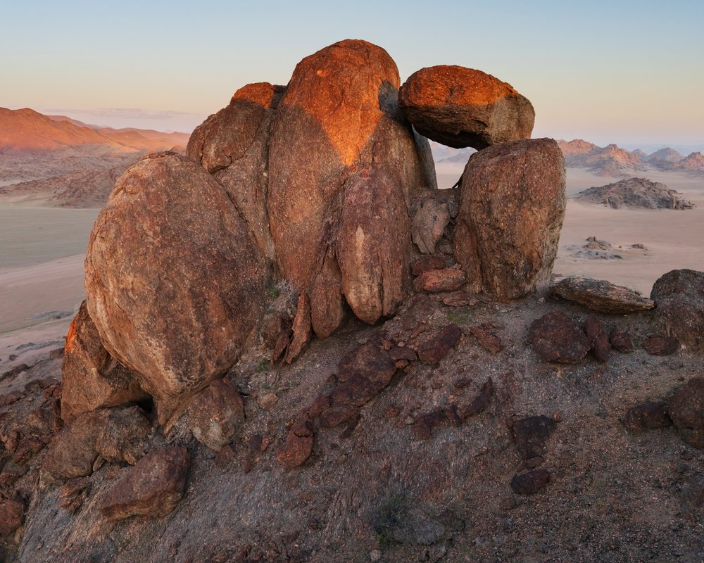 Large natural balanced rock formation illuminated by warm Sunset light in rocky arid terrain with distant mountains in Stone Valley, landscape, wildlife, Purros, Kunene Region, Namibia.