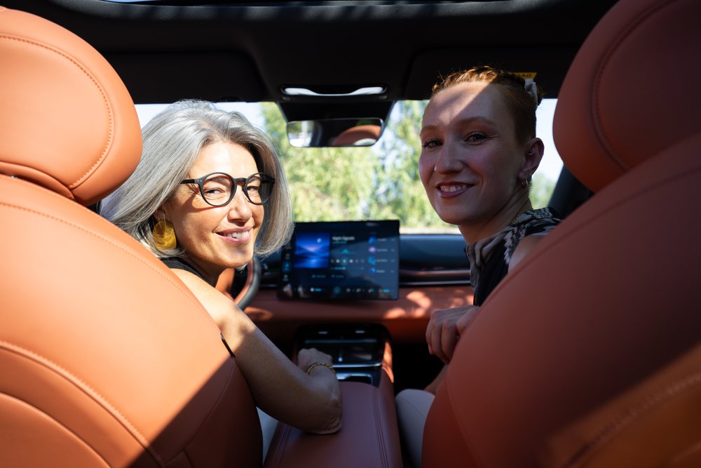 Two adult women smile and look back inside a modern car with brown leather seats in Spain during daylight, businesswomen.