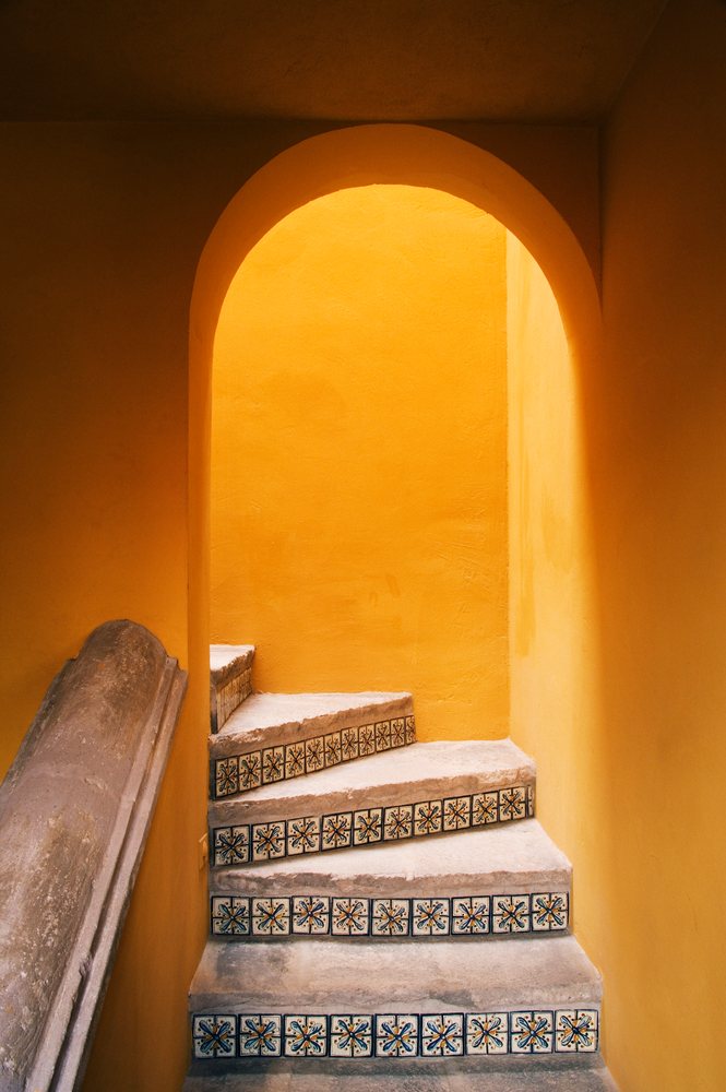Interior stairway featuring decorative patterned tiles on risers with an arched doorway and orange walls in a Mexican house, Mexico, San Miguel.