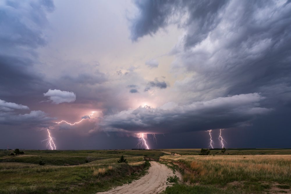 Lightning bolts from a Supercell storm illuminate dusk over rural grasslands and a dirt road, Wallace, Nebraska, USA.