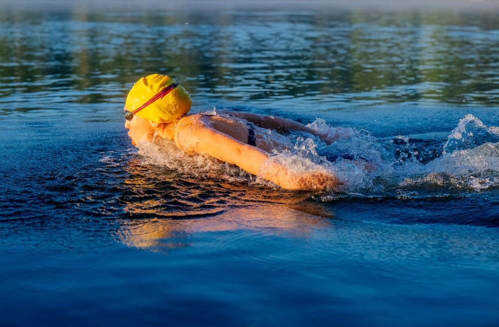 Swimmer wearing a yellow swim cap and goggles performing freestyle stroke in open water, USA.