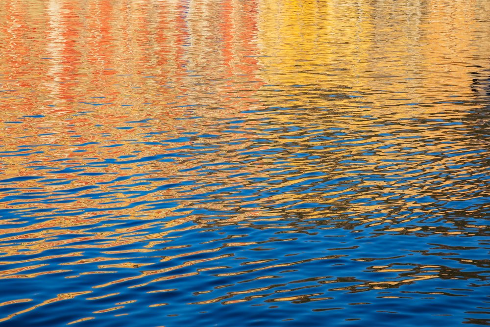 Ripples and colorful reflections in vibrant orange, yellow, and blue hues appear on the water surface, Travel Photography, Bastia, Corsica, France.