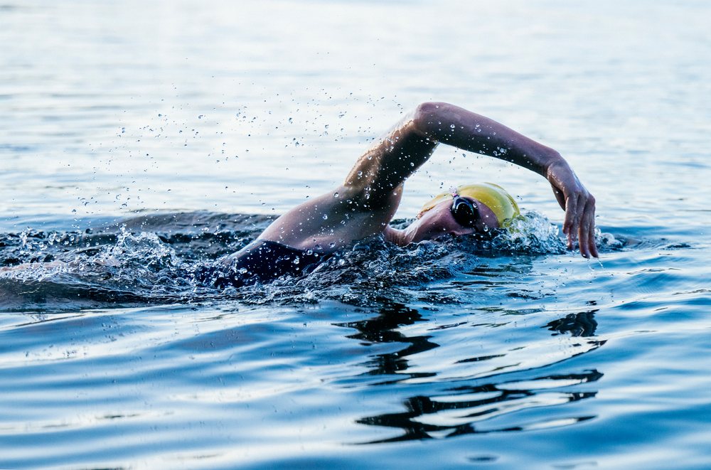 Person performing freestyle stroke in open water wearing a yellow swimming cap and goggles, USA.