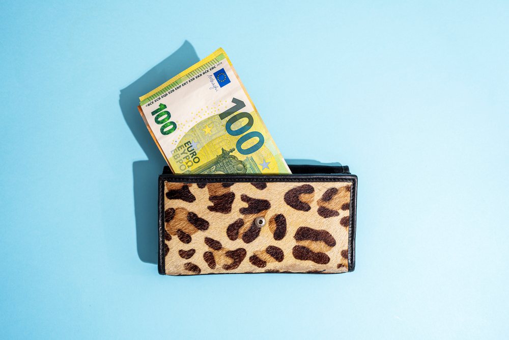 Open leopard print wallet holding multiple 100 euro banknotes on a blue background in a studio setting, Studio Shot.