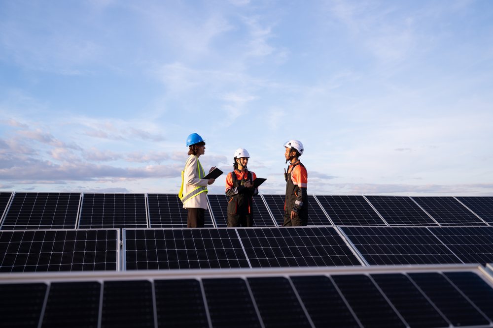 Engineers inspecting solar panels outdoors at a solar energy site, Spain under clear blue sky, Madrid.